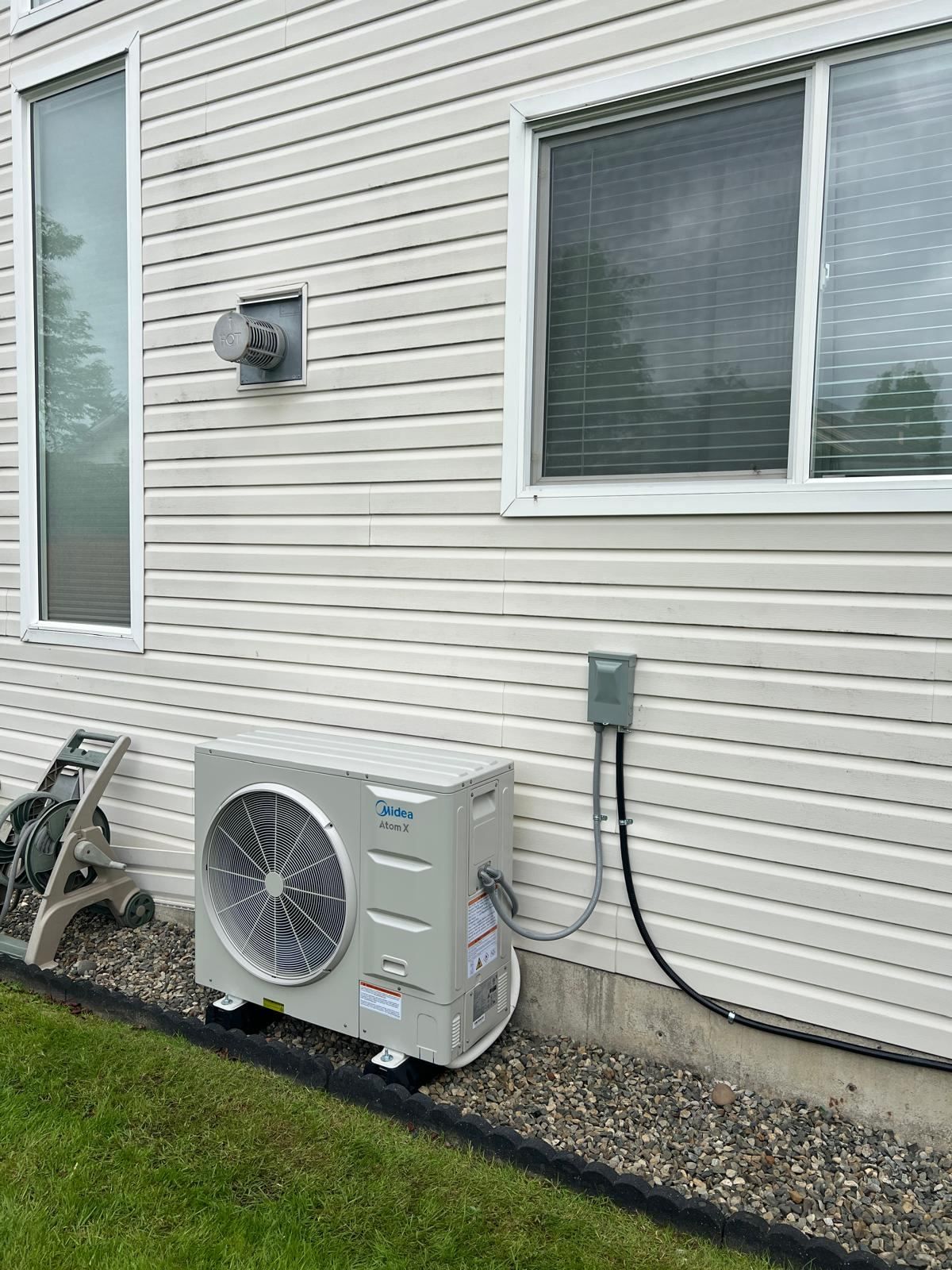 Midea Atom X outdoor heat pump condenser installed beside house with electrical disconnect